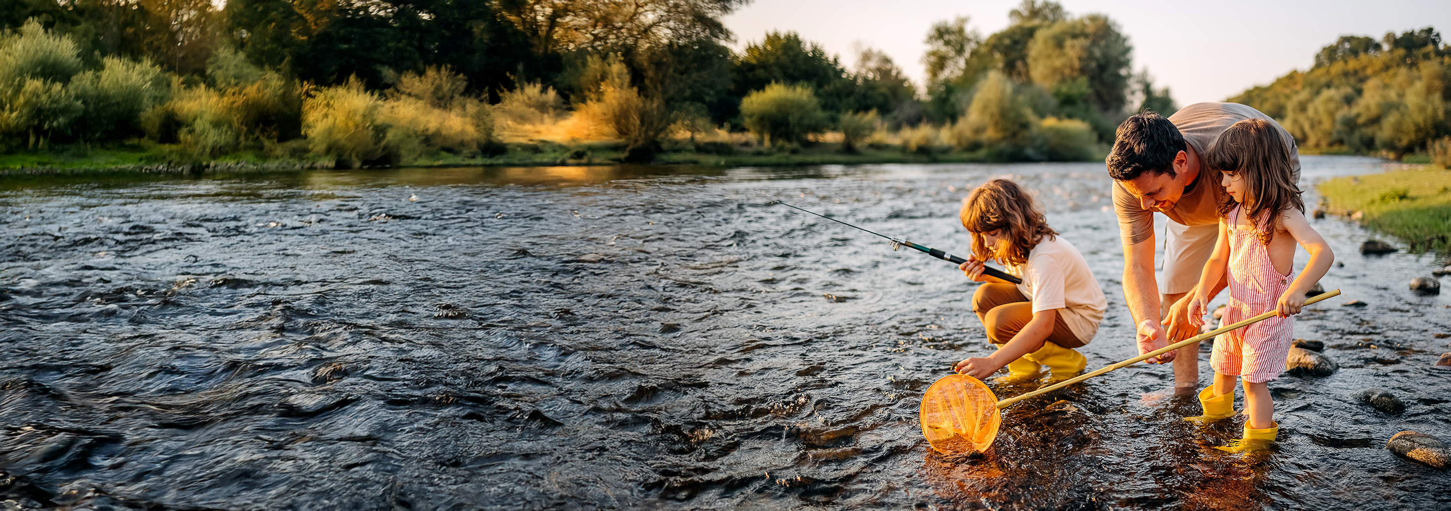 man fishing in a river with his two young daughters at sunset