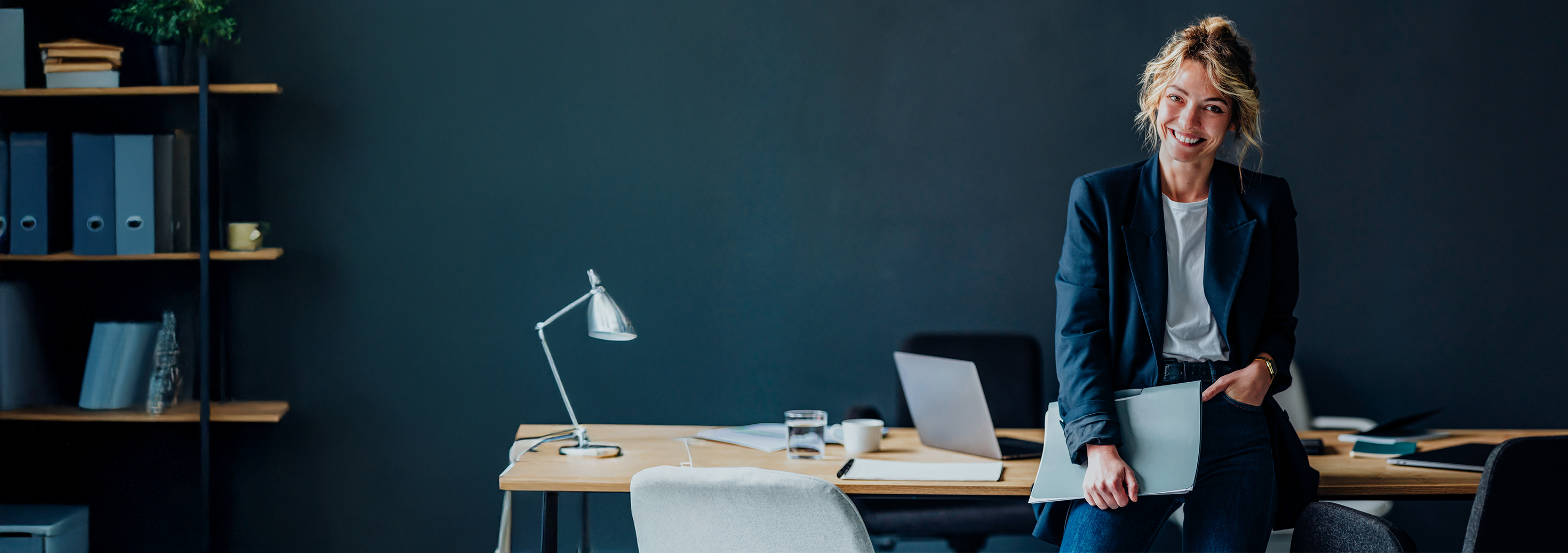 Woman smiling holding a folder leaning against her desk