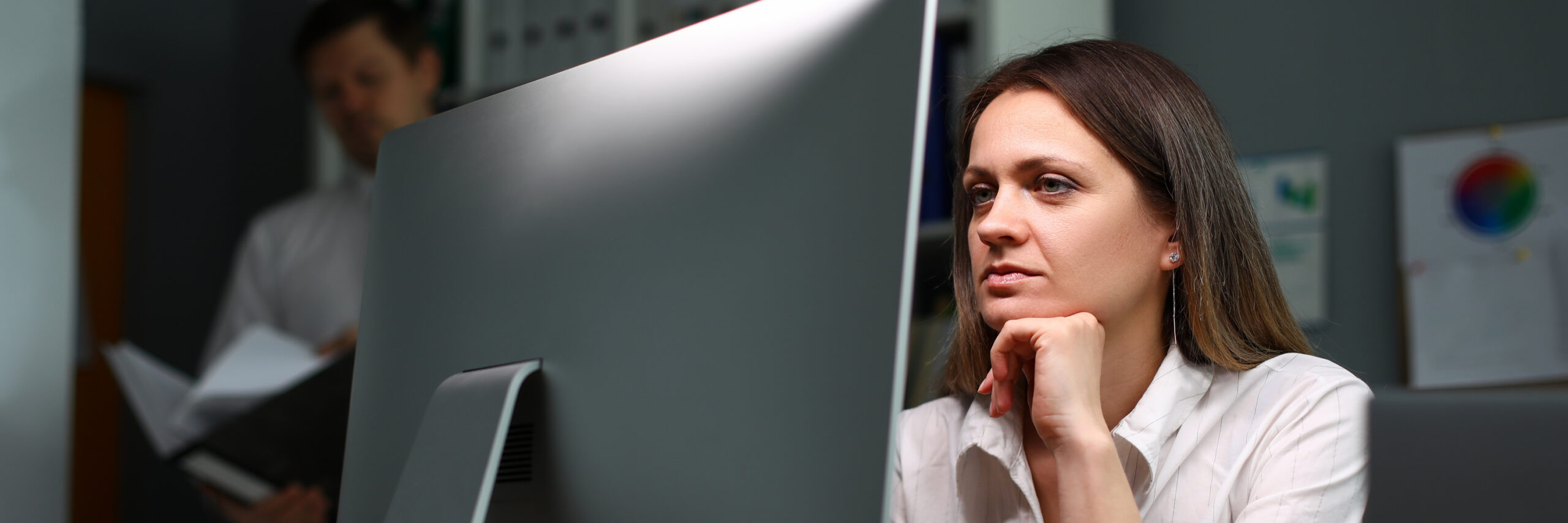 A woman sits at her computer, reading something with a serious expression.